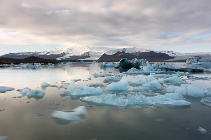 Glacial lake with floating ice blocks and snowcovered mountains in the background beneath a cloudy sky