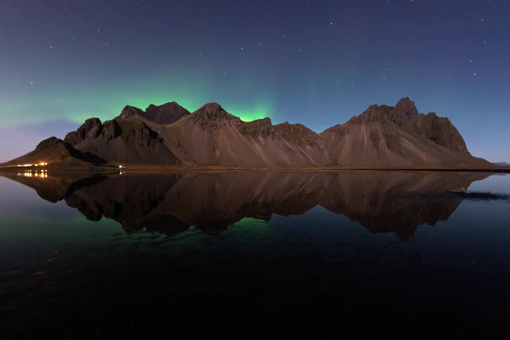 Mountains reflected in a calm lake with a soft northern lights glow in the night sky