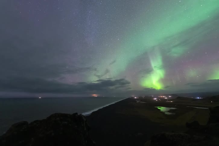 Mountains and houses along the coast as the aurora borealis glows among stars in the sky
