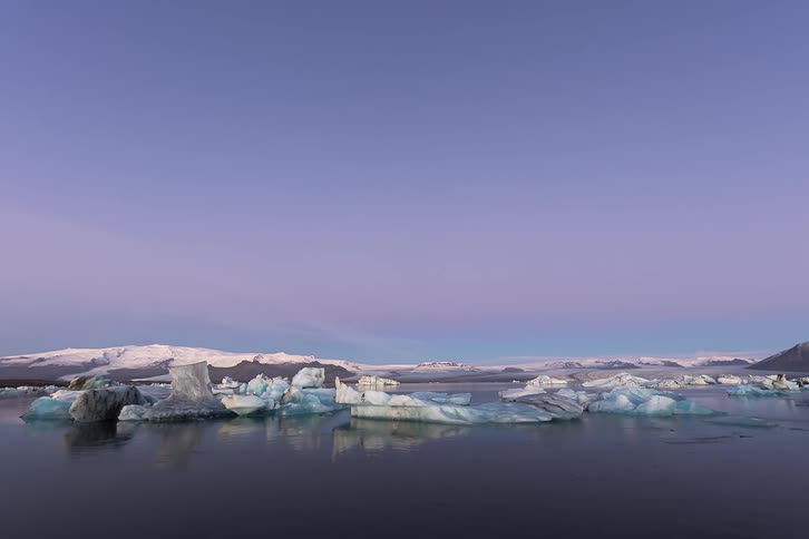 Dawn over a glacial lake with floating ice blocks and mountains in the background under a clear sky