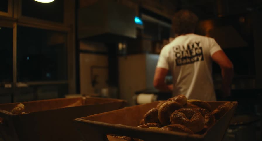 A baker working in a commercial bakery production area surrounded by bread racks and machinery