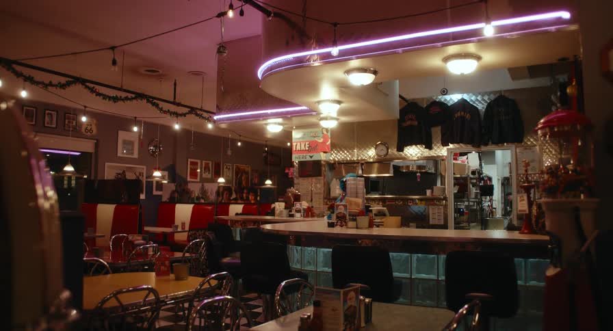 An empty retro style diner interior at night glows with neon lighting over booths and a central counter
