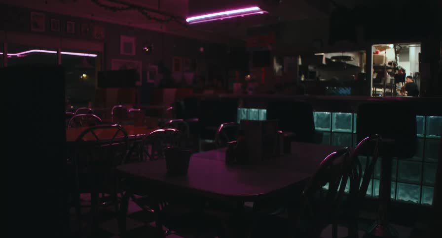 Empty diner with aligned tables metal chairs neontoned lighting and a counter in the background