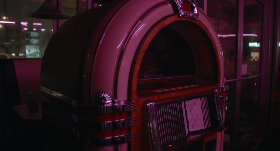 A vintage jukebox stands indoors illuminated by pink and purple lighting