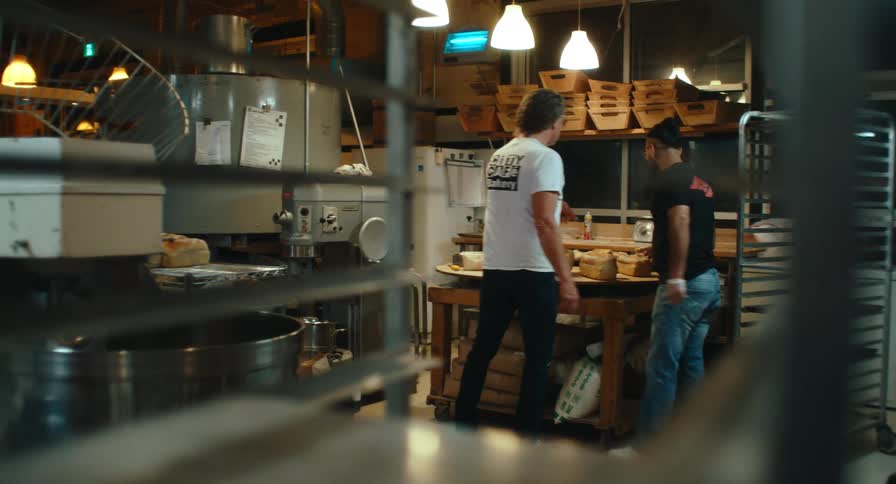 Two men work with freshly baked loaves of bread at a table in a commercial bakery