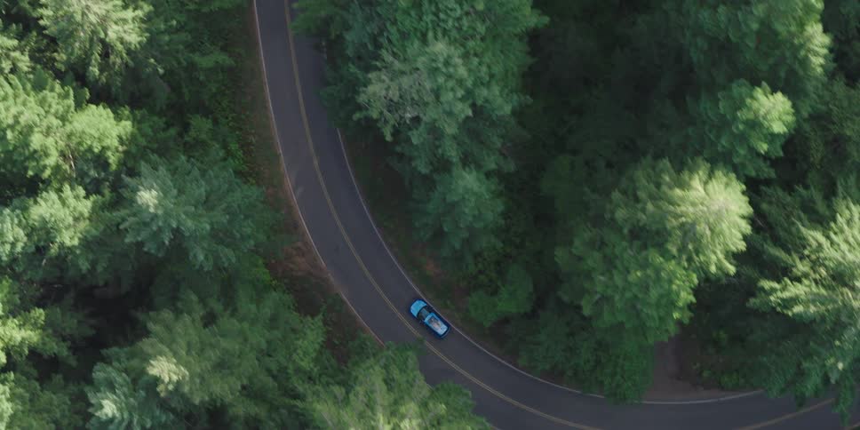 The car is driving through the woods on a winding road