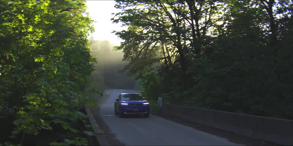 Sun glares through the trees on a foggy day as a vehicle crosses a bridge in the woods
