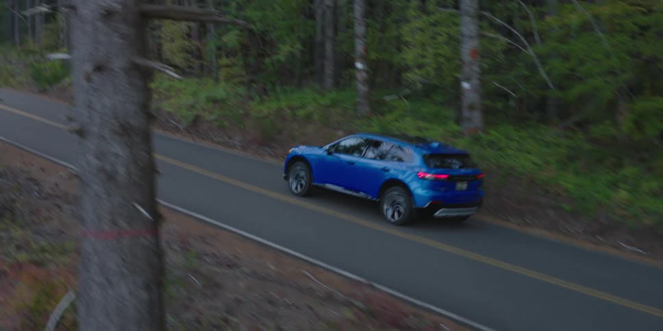 A blue sedan drives on a remote road in an evergreen forest