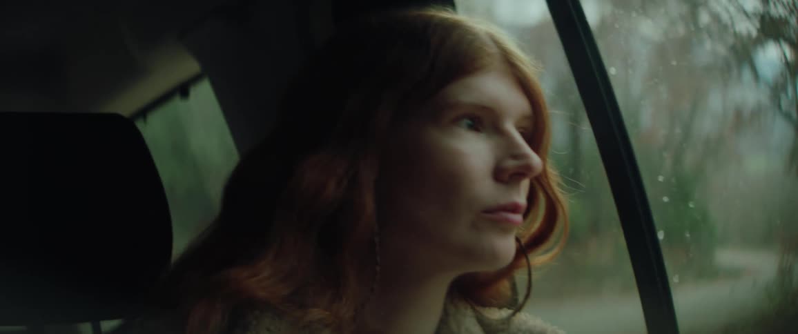 Young adult woman sitting inside a car looking out of the window with a contemplative facial expression during day time