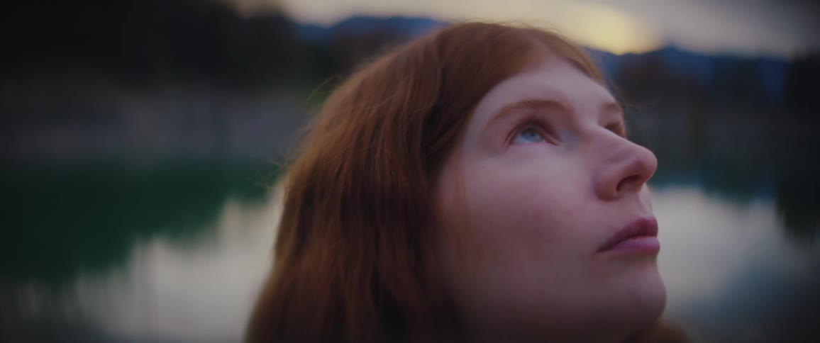 A woman with long red hair stands outside and looks up at the sky