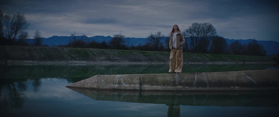 Young woman walks on a concrete barrier in a reservoir overlooking the water with mountains in the distance