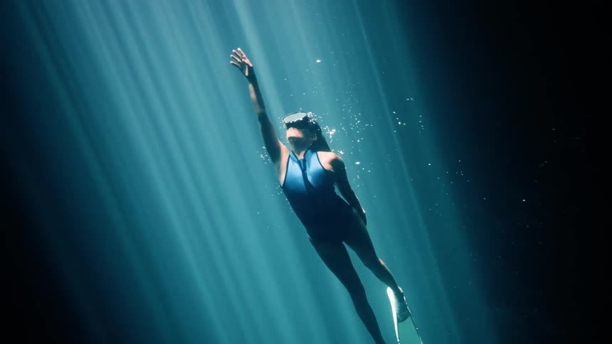The woman is swimming towards the surface of the water