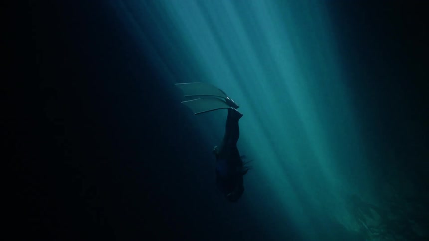 A person scuba diving deep on the ocean floor as a stream of light shines down illuminating part of the dark water