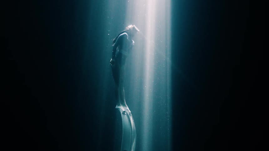 The woman is swimming up towards the light