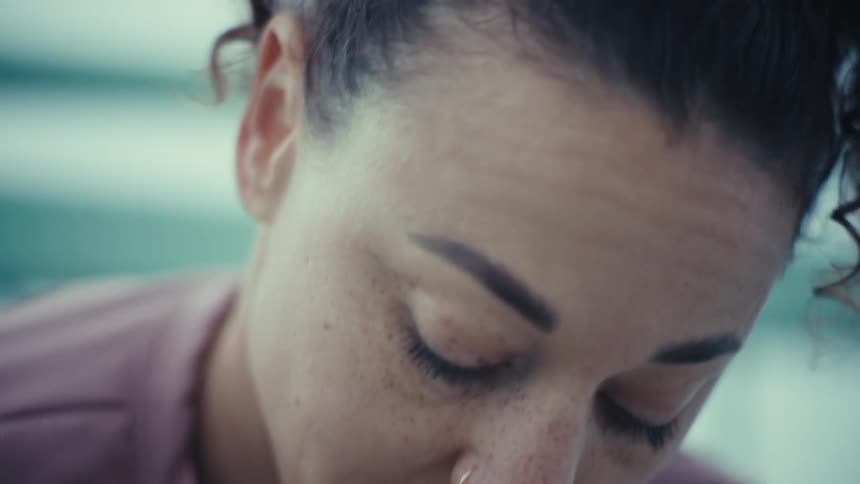 A young woman wearing a pink longsleeve tshirt squatting to tie her shoelaces as she prepares to go for a jog at midday