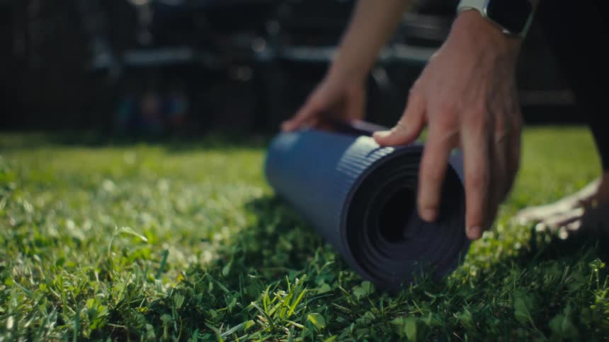A person rolls out a rolledup yoga mat on sunlit grass capturing a quiet moment of calm and readiness before movement begins