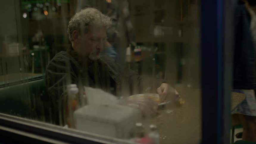 A curly haired man eats at a restaurant