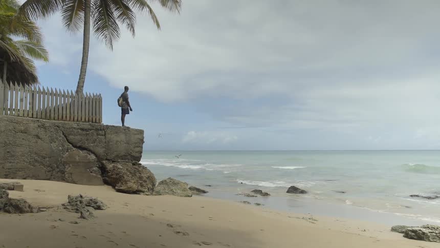 A man stands on a stone wall and looks out at the ocean