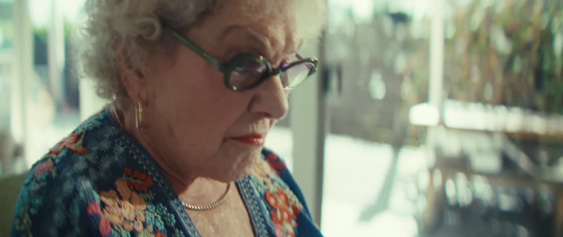 An elderly woman wearing glasses meticulously reviews data charts on paper