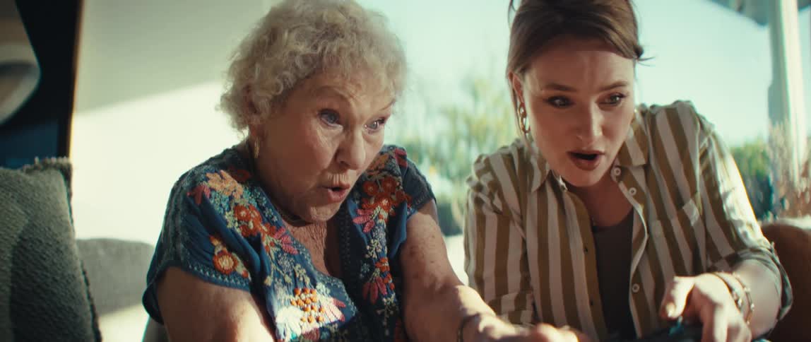 Elderly woman and her granddaughter sitting on a couch playing video games on a tablet computer as they move the controllers in excitement