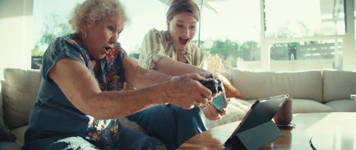 Two women sitting on a couch in the living room each holding a controller and playing a video game having fun at midday