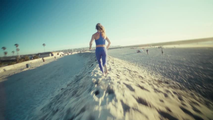 A young woman running barefoot on a sandy beach barrier at sunset