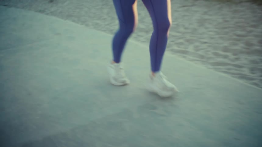 A pregnant woman in blue athletic gear runs along a beachside path during a sunny day she maintains a steady pace while wearing white sneakers and a fitness tracker on her wrist