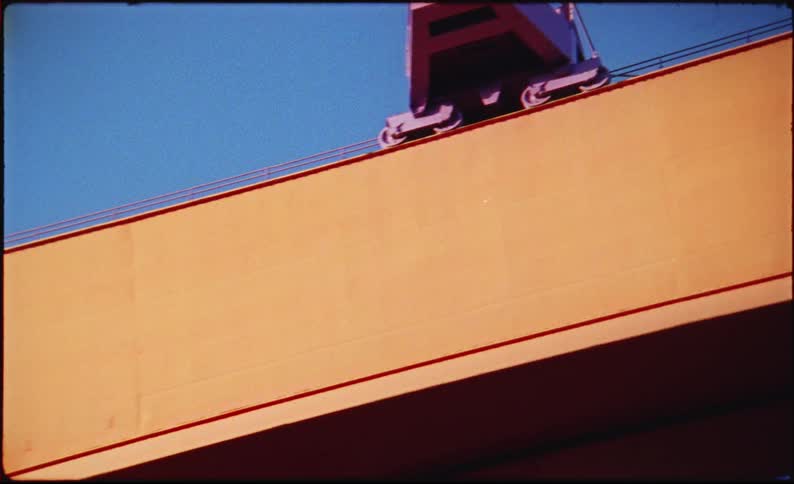 Orange ship hull with large white letters and metal gangway under blue sky