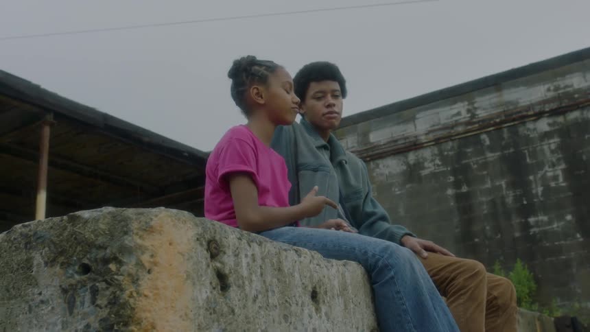 A boy and girl sit on a concrete wall and talk
