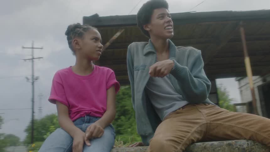 Teen boy and young girl sitting and talking outdoors on a cloudy day