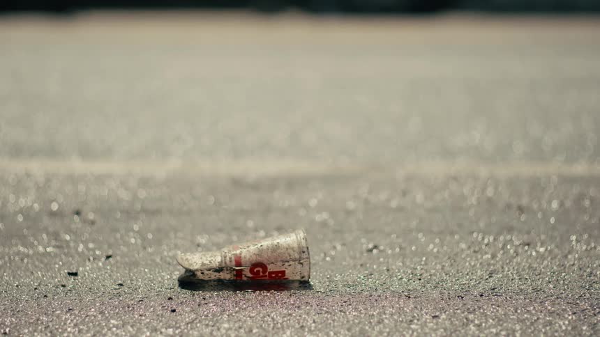 Traffic passes a partially crushed disposable cup lying on the asphalt during the daytime
