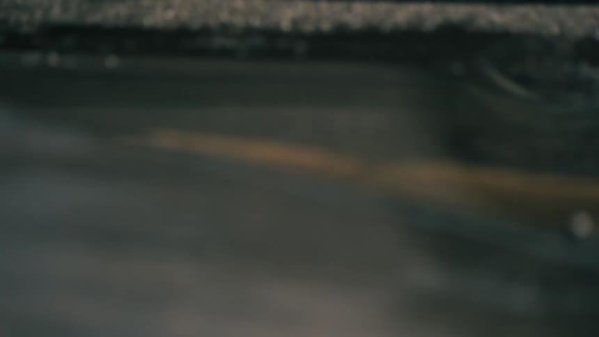 A blurry reflection of vehicles appears in a shallow puddle on a gray asphalt surface during an overcast day