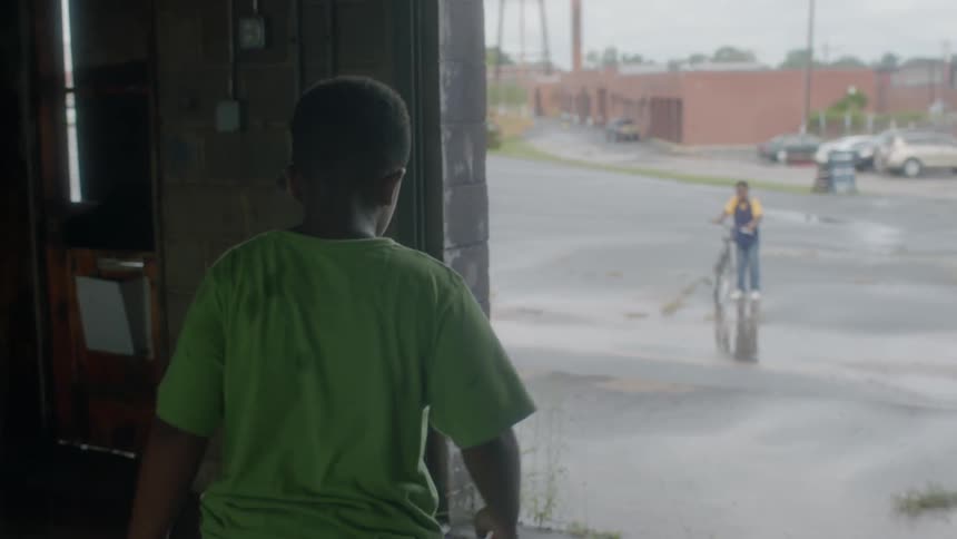 A boy in a green shirt walks on a wet driveway