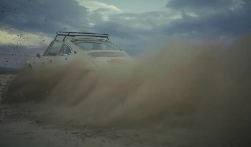 White car skids across sandy ground kicking up mud and debris