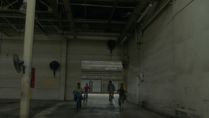 Kids ride their bicycles around a corner in a warehouse