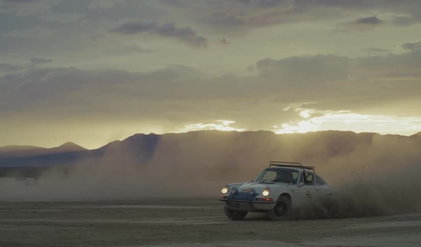 A man is kicking up dirt as he drives his car in circles in the desert
