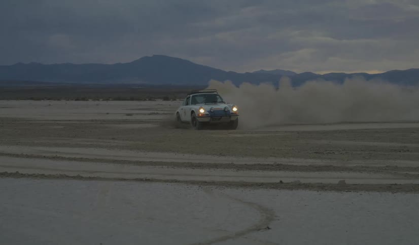 Car travels on snow and ice leaving a trail of smoke behind as it turns and slides with mountains in the distance
