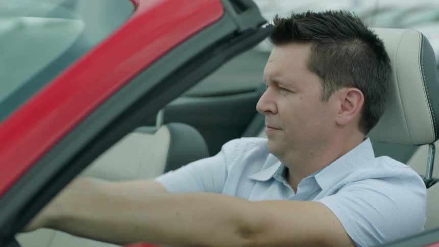 A man sitting in a car looks happy as he drops the convertible top