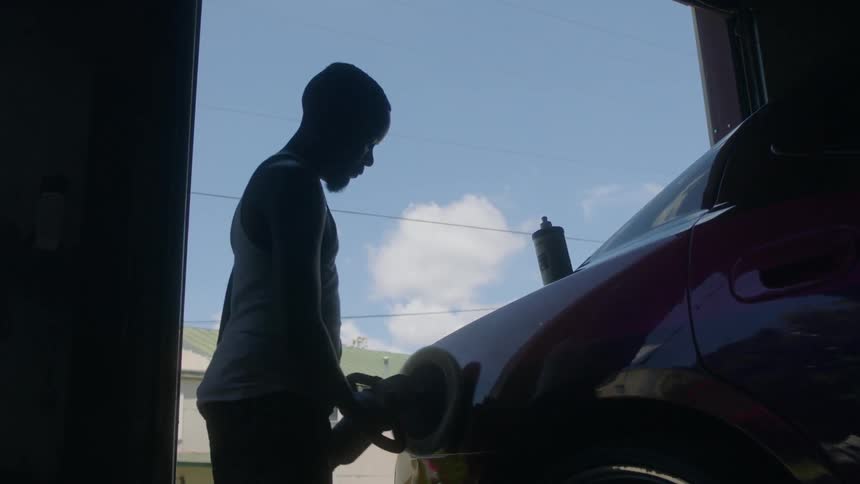 A man uses a buffer on a car fender