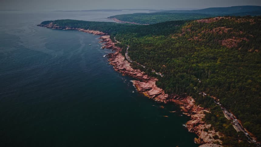Aerial view of a forested mountain landscape with a road and buildings overlooking the coast