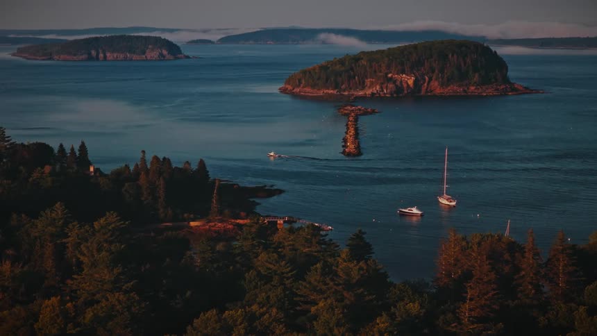 Boats between a forested coast and an island on a foggy day