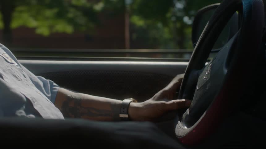 A man with tattoos drives a car on a sunny day