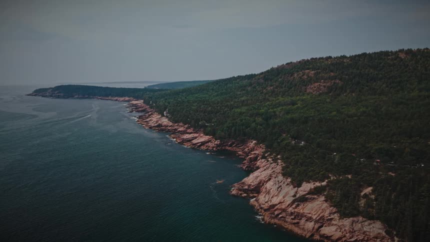 Aerial view of a forested mountain landscape with a road and buildings overlooking the coast