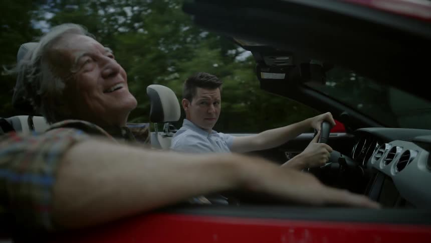 Older man smiles while riding as passenger in convertible car