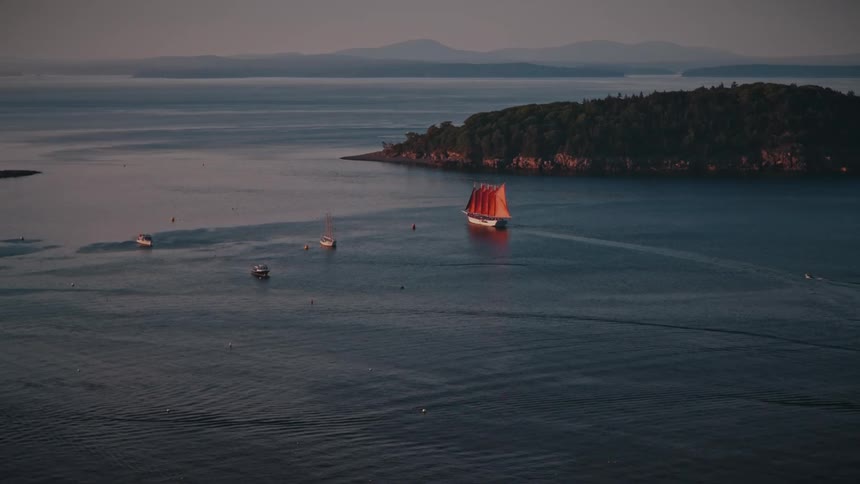 Sailboat with orange sails sailing near an island