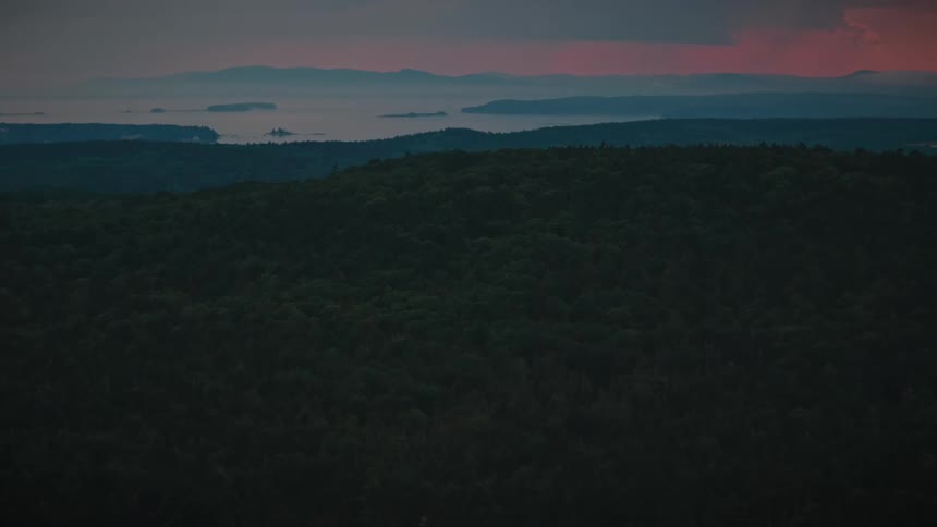 Forest area on highlands next to the ocean with a mountain range on the other side outdoors during dusk or dawn