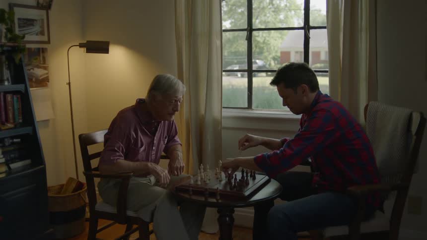 Two men sit in a living room playing chess