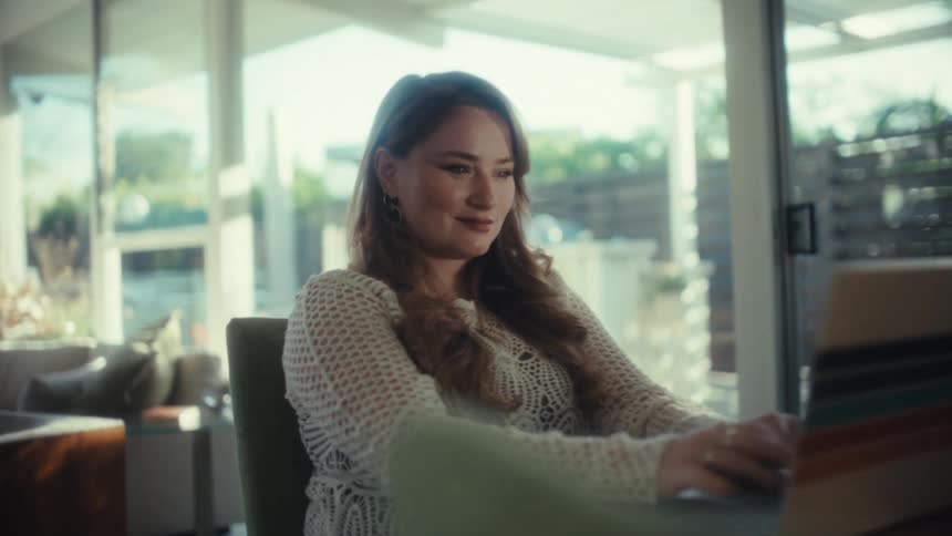 The woman smiles while typing on her laptop