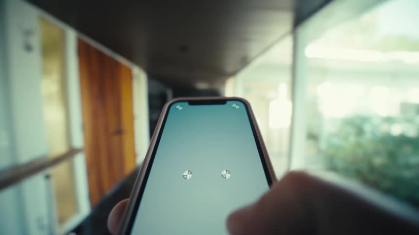 A close view shows a hand holding a smartphone with tracking markers on the screen while walking through a modern house with large windows and wooden doors