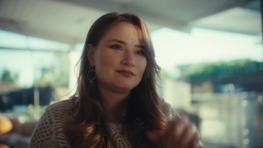 Young woman sitting at a table closing the lid of a laptop computer and pauses to think